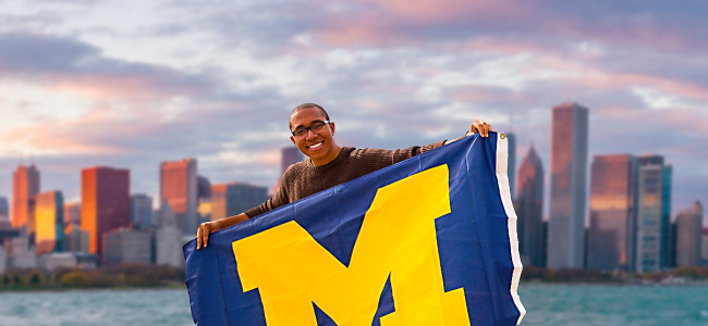 student with Chicago skyline in background holding UM flag