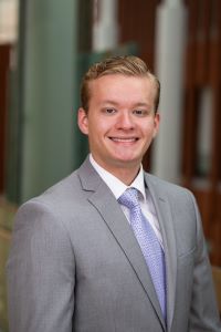 Photo of Michigan Ross BBA student Alexander Apetroaei. He is wearing a light gray suit jacket with a white button shirt underneath with a light purple tie. He is smiling. 