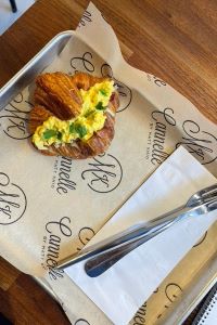 Photo of a Cannelle croissant with egg stuffed in it with a fork and knife on a napkin next to it. 