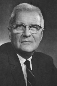 Black and white photo of a man wearing glasses and a dark suit