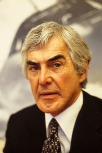 Photo of John Delorean, man with gray hair and dark eyebrows wearing a black suit with a white shirt.