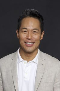 Photo of Richard Lui with dark hair smiling and wearing a tan suit jacket with a white shirt.