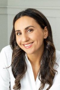 Photo of Yumna Jawad with long dark hair wearing a white shirt and smiling 