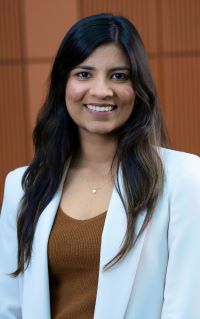 Photo of Michigan Ross Weekend MBA student Devinaa Mangal wearing a light blue jacket with a brown shirt underneath. She has long dark hair and is smiling. 