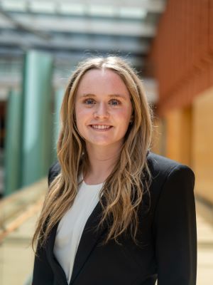 A woman with long blonde hair smiles, wearing a black blazer and white shirt in the Ross Winter Garden
