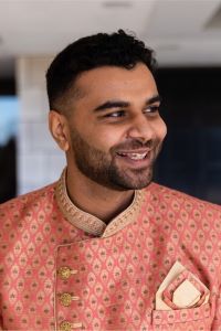 Photo of Hardik Tripathi Michigan Ross Weekend MBA student. He is wearing a traditional Indian jacket that is red and gold. He has dark hair and is smiling. 