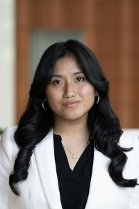 Photo of Jasmine Mucha-Nonalaya, a Michigan Ross BBA student. She has long dark hair and is looking at the camera and smiling. She is wearing a white suit jacket with a black shirt underneath.