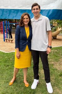 Photo of Michigan Ross BBA student Karim Kadouh standing next to Michigan Governor Gretchen Whitmer. He is wearing a white short sleeve shirt and black pants with white tennis shoes. The woman is wearing a yellow dress with a navy blue blazer over the top of it. She has dark hair that is medium length. They are both looking at the camera and smiling. 
