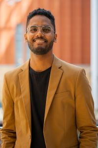 Photo of Khalid Hamdan, Michigan Ross BBA student, wearing a brown jacket with a black shirt. He has short dark hair and is wearing glasses and smiling. 