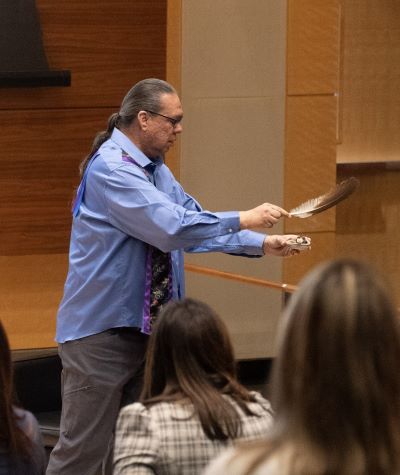 A man in business attire holds a feather as he performs the smudging ceremony onstage in the Robertson Auditorium.