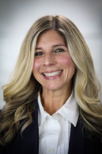 Photo of Michigan Ross Executive MBA student Nicolle Marinec. She has medium length blond hair and is wearing a black suit jacket with a white button down shirt underneath. She is smiling.