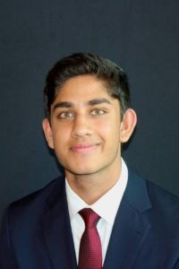Photo of Michigan Ross BBA student Nilay Mishra. He is wearing a black jacket with a white shirt underneath with a red tie. He has dark hair and dark eyebrows and he is smiling.