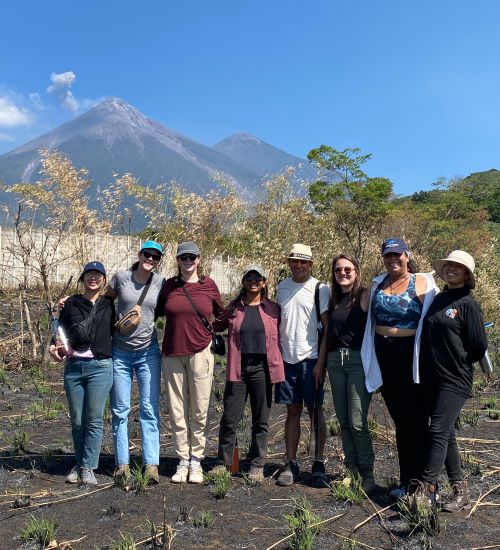 Students stand near a large smoking volcano