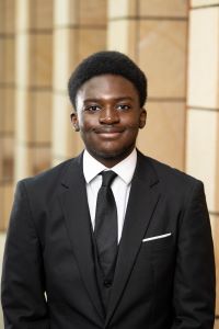 Photo of Michigan Ross BBA student Stephen Asante. He is wearing a black suit jacket with a white shirt underneath with a black tie. He has short dark hair and is looking at the camera and smiling.