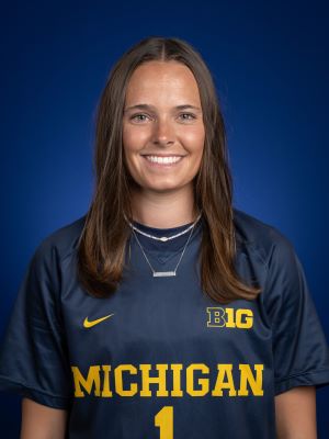 A woman with shoulder-length brown hair smiles, wearing a maize and blue jersey that reads "Michigan #1"