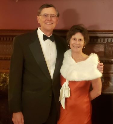 A couple smiling, dressed formally in a suit and dress