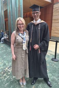 Photo of Nathaniel Gallegos Michigan Ross Executive MBA graduate. He is wearing a graduation cap and gown. He is standing next to a woman wearing a brown dress with blonde hair. They are both wearing glasses and smiling. They are standing in the Michigan Ross Winter Garden.