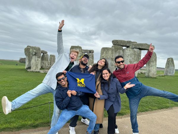 Students do dynamic and goofy poses with a Ross flag in front of Stonehenge