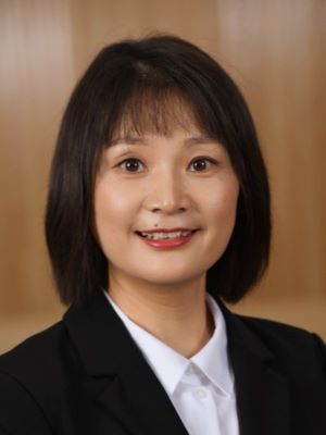 Hong Chen poses in a black blazer in front of a wood background