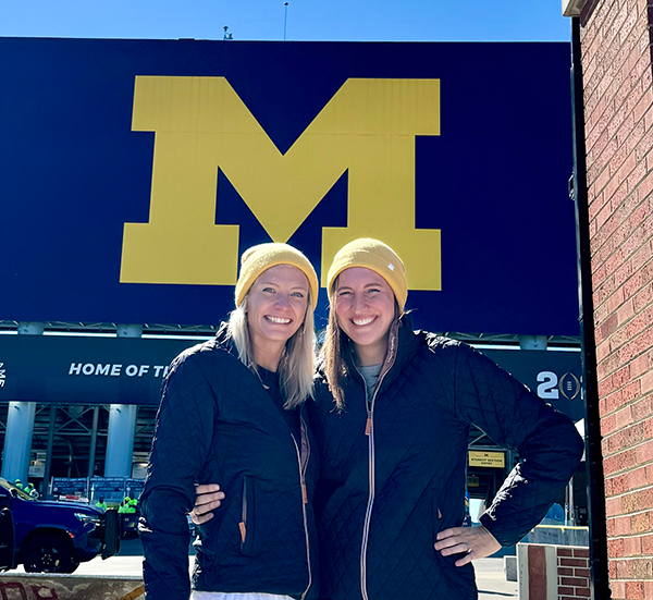 The two alums standing together in blue coats in front of the Big House in Ann Arbor.