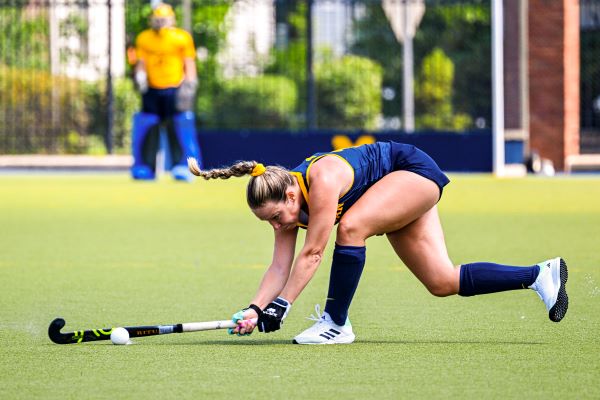 A woman lunging forward to hit a ball on a grassy field