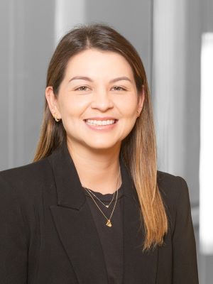 A woman with long brown hair and a black blazer smiling in a bright room
