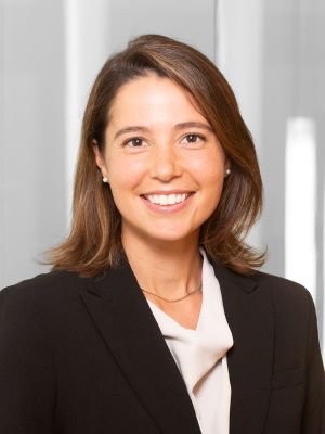 A woman with short brown hair and a black blazer smiling in a bright room
