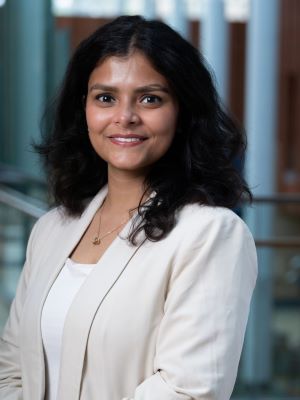 A woman with shoulder-length dark brown hair smiles wearing a white blazer and shirt in the Ross Winter Garden