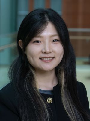 A woman with long dark hair and a black blazer on smiling