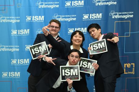 The team poses with ISM papers in their hands, making silly faces in front of an ISM background
