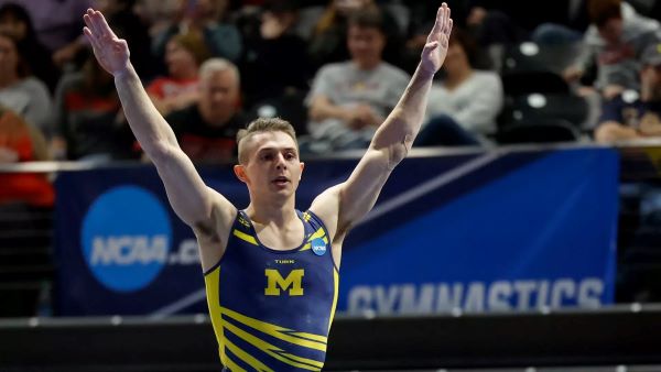 Paul Juda posing with arms in the air at a gymnastics event in front of a large audience