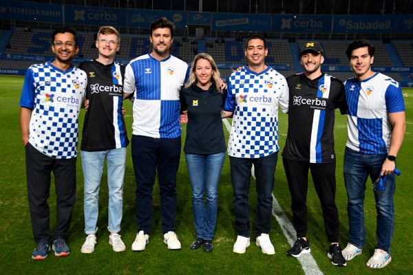 The team stands on a futbol pitch wearing the team uniforms of Sabadell FC