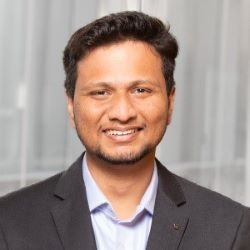 Sai smiling in a gray suit in front of windows in the Ross building