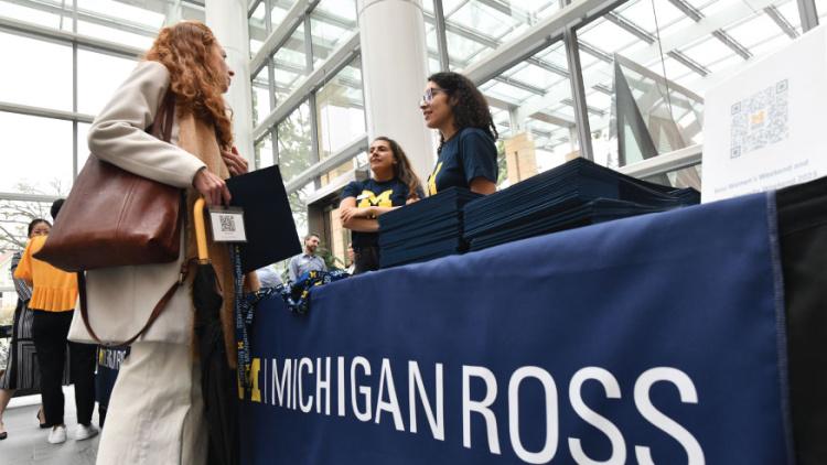 A table that says Michigan Ross surrounded by an interested student and two admissions representatives