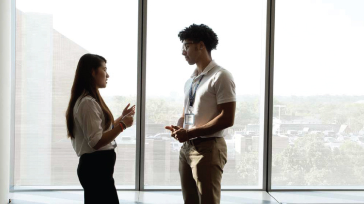 Two people talking in a hallway in front of large windows