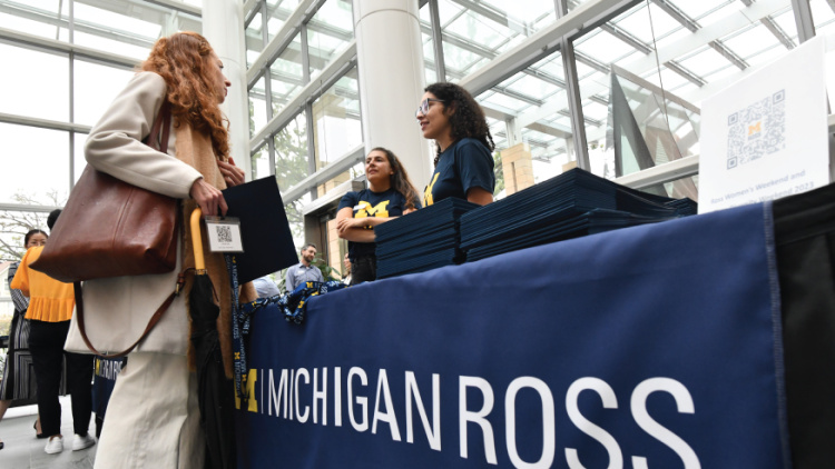 Two women talk at a registration table with a Michigan Ross banner.