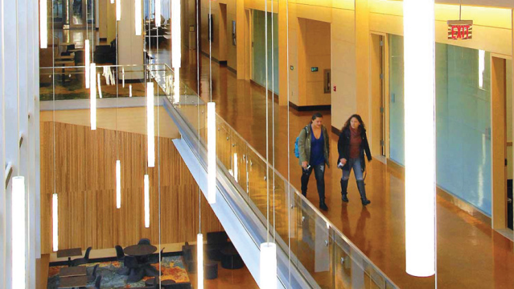 Two people walking down a brightly lit hallway in the Ross building.