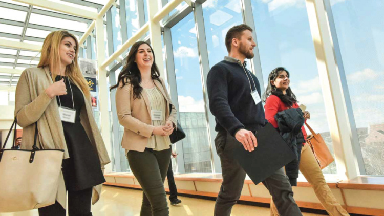 Four adults walk together in a bright hallway wearing conference badges.