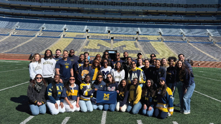 Group of people posing together on a football field in a stadium with yellow seats.