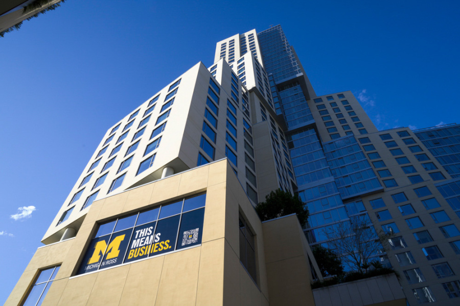 A modern high-rise building against a clear blue sky, featuring large windows. A sign reads "This Means Business" with a bold letter "M".