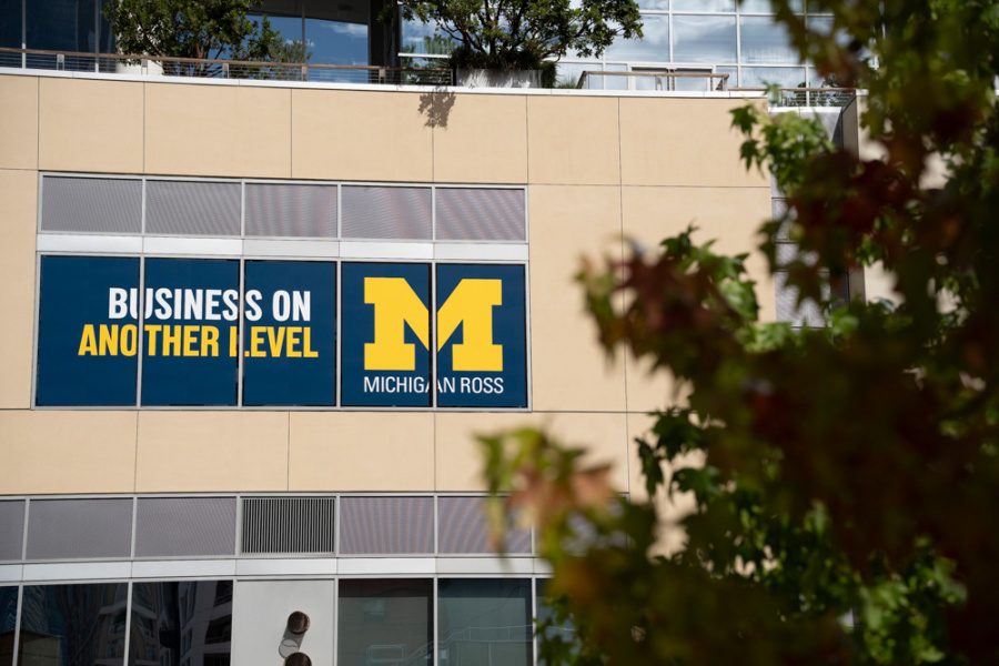 The image shows a beige building facade with a large sign reading "BUSINESS ON ANOTHER LEVEL" and a prominent yellow "M" for Michigan Ross. Trees frame the view.