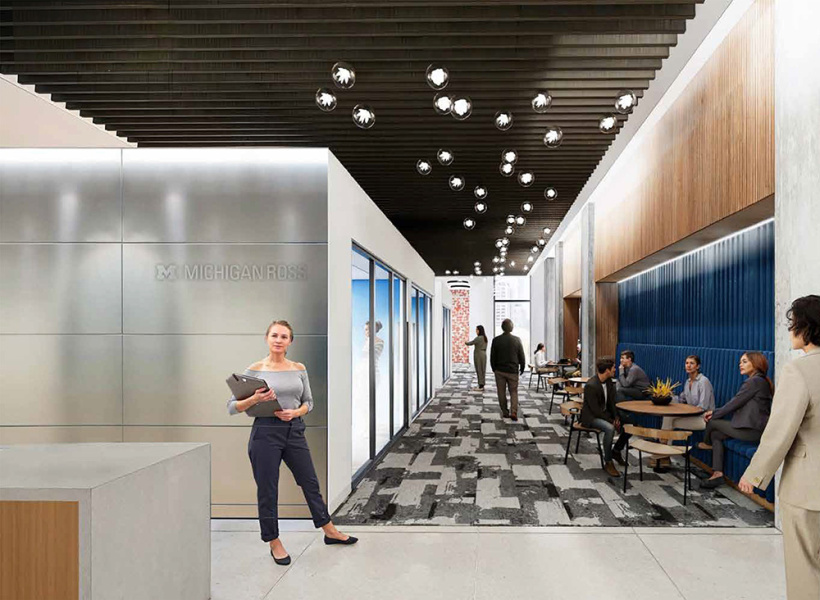 Modern office lobby with sleek design. A woman holds a laptop on the left, while people chat at tables on the right. Hanging lights and patterned carpet add style.