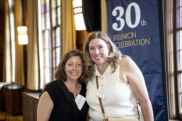 2 people pose for a photo in front of 30th reunion banner