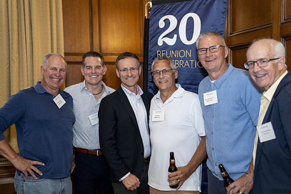 6 people pose together for a photo in front of 20th reunion banner