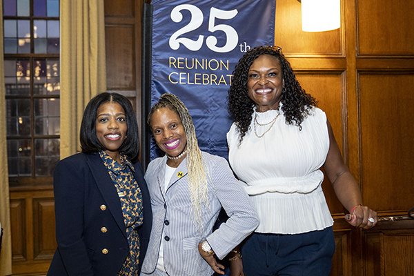 3 people pose together in front of 25th reunion banner