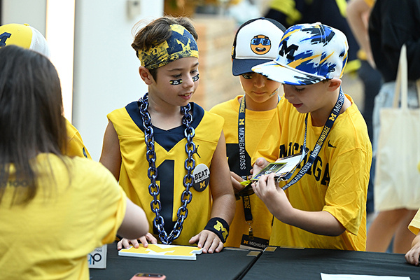 3 kids show each other their badges while wearing U of M apparel 