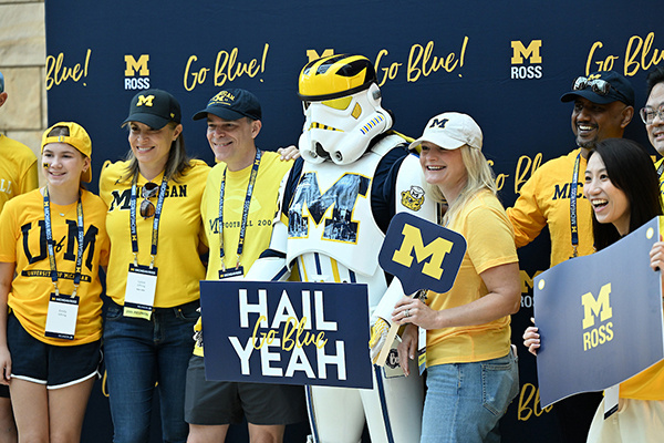 people pose with a "U of M Stormtrooper" in front of a step and shoot U of M backdrop