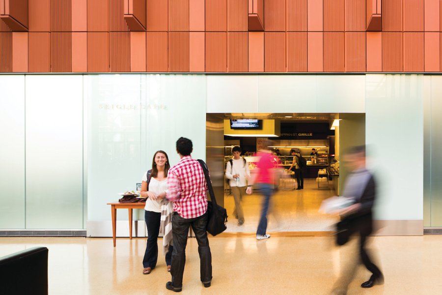 People walking in and out of a modern building lobby with a reception desk.