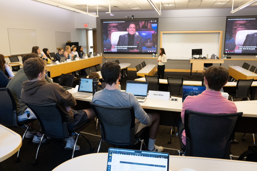 Students in a modern classroom watch a large screen as an instructor gives a lecture.