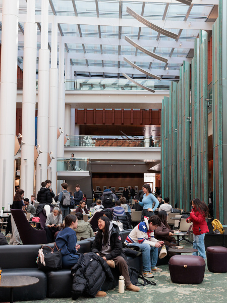 Students gather and study in a bright, modern indoor common area with large windows.